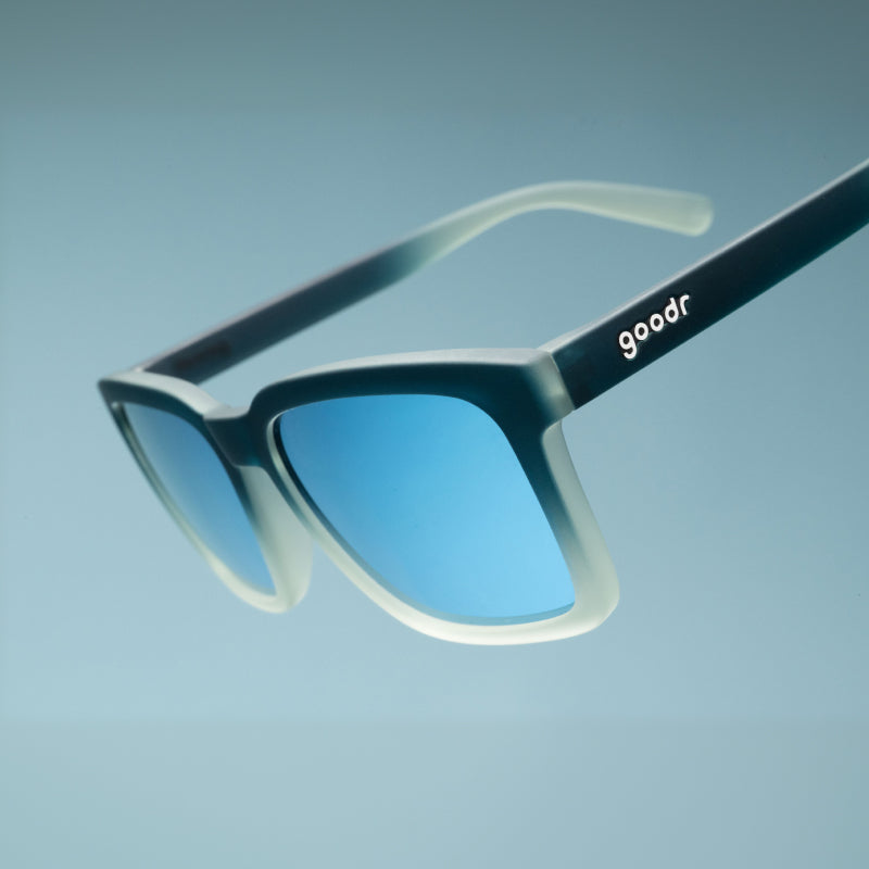 Angled close-up of translucent black & teal shades w/ blue reflective lenses & a classic square silhouette tilted down.