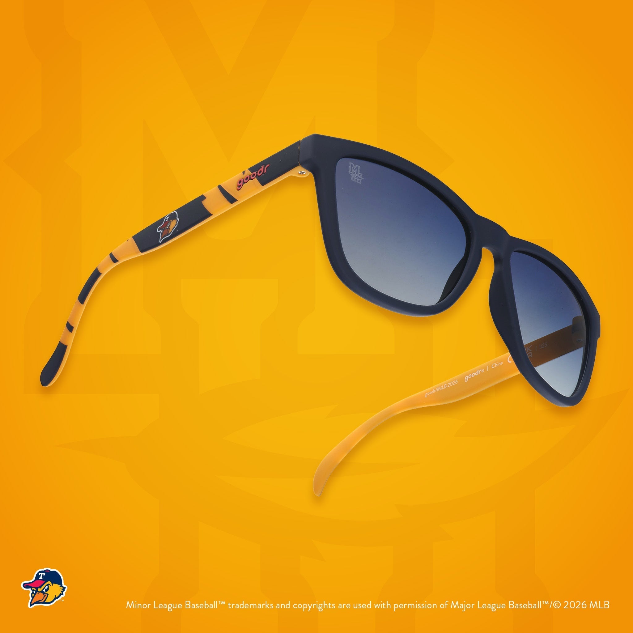 Three-quarter angle view of shades. Blue frames w/ a yellow pattern, Mud Hens logo on temples + blue gradient lenses.