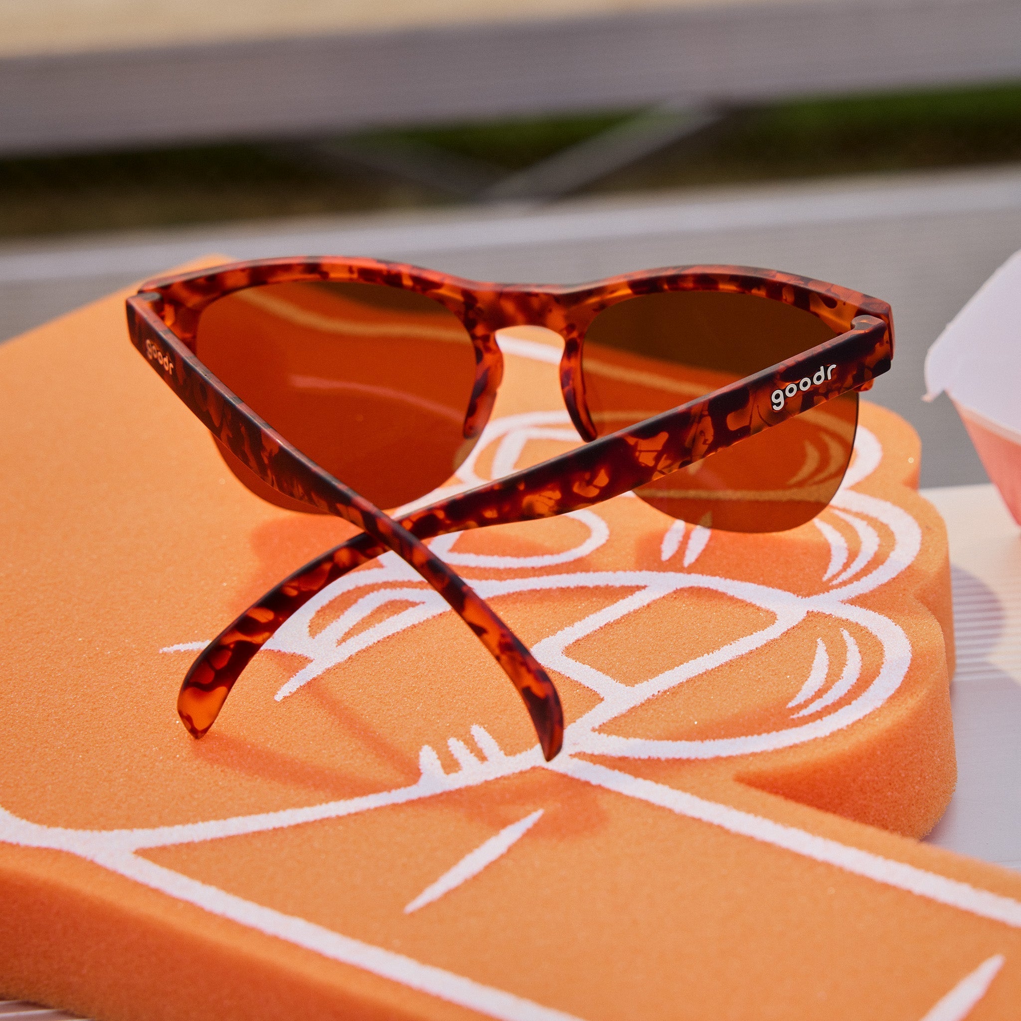 Side angle view of stylish brown tortoiseshell half-rim sunglasses with brown non-reflective lenses atop bleachers.