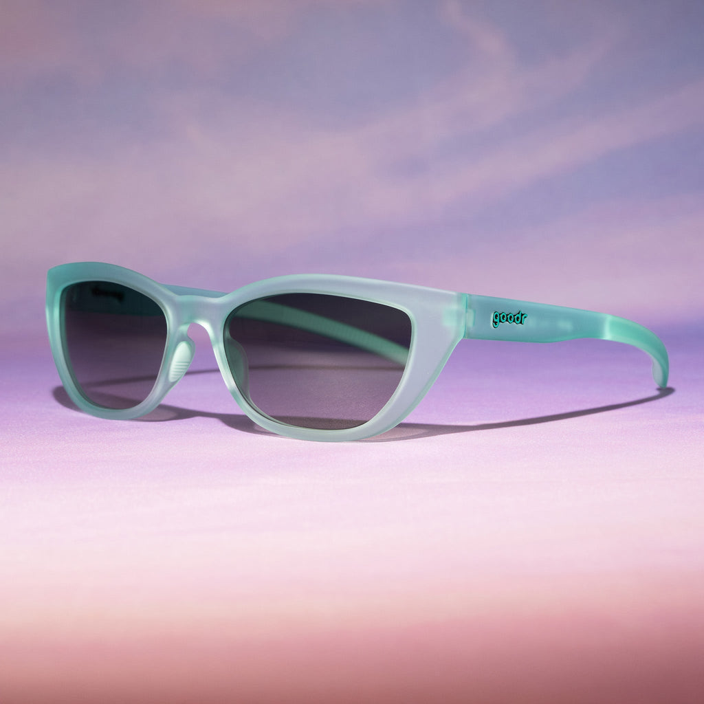 Three-quarter angle view of translucent pale green Cheetah Gs with green gradient lenses on a pinky peach ombre backdrop.