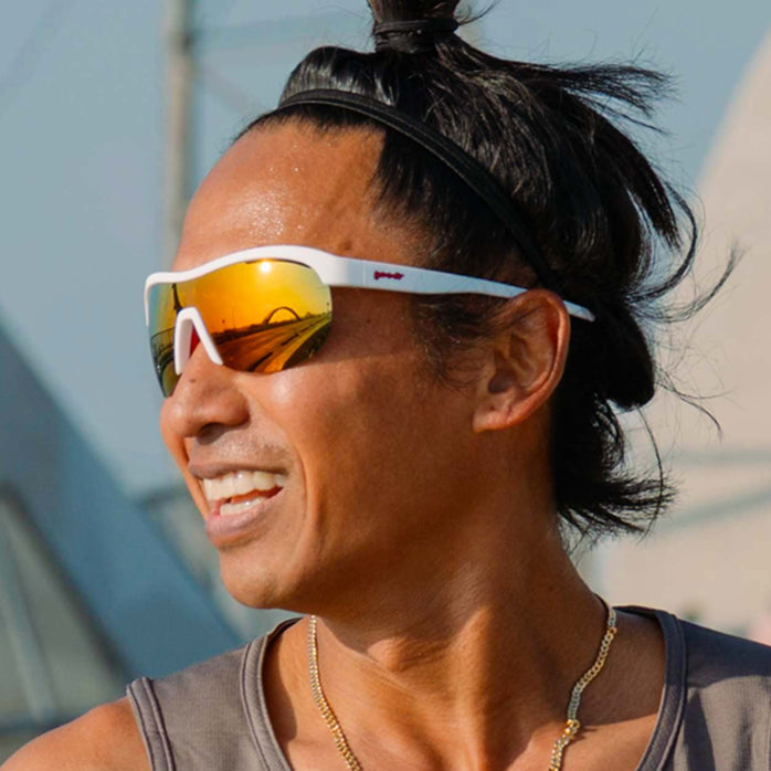 Model smiling while wearing white wrap shield sunglasses with red accents and fire-red reflective lenses.