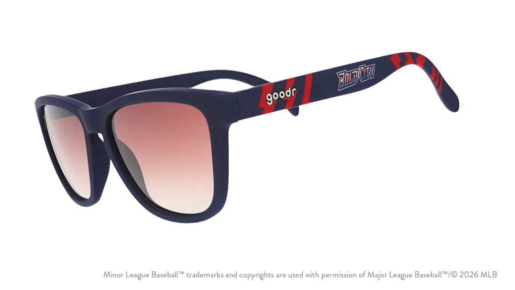 Three-quarter angle view of shades tilted down. Blue + red frames w/ Bold City on temples. Brown gradient lenses.