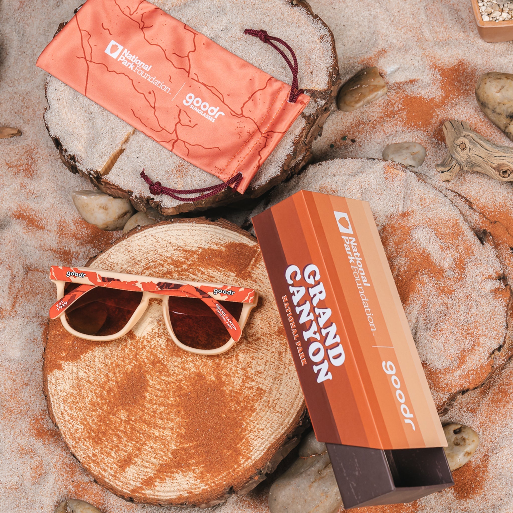 Grand Canyon National Park sunglasses, featuring a mountain silhouette design in shades of orange, brown, and peach. Next to the sunglasses is the goodr box and sunglass sleeve/pouch, all with a matching color/design scheme.