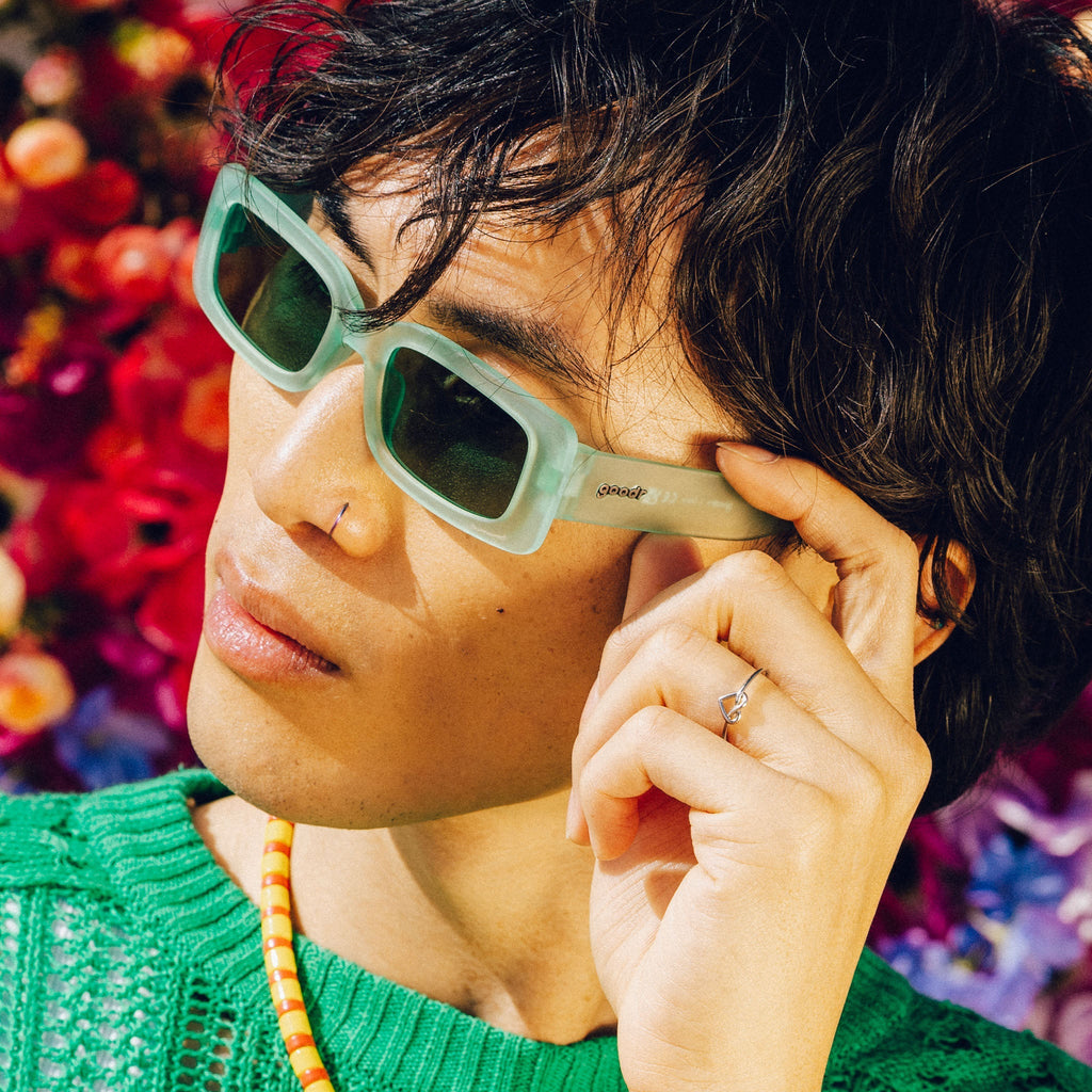Left profile of a man wearing and posing with light green rectangular sunglasses with green lenses.