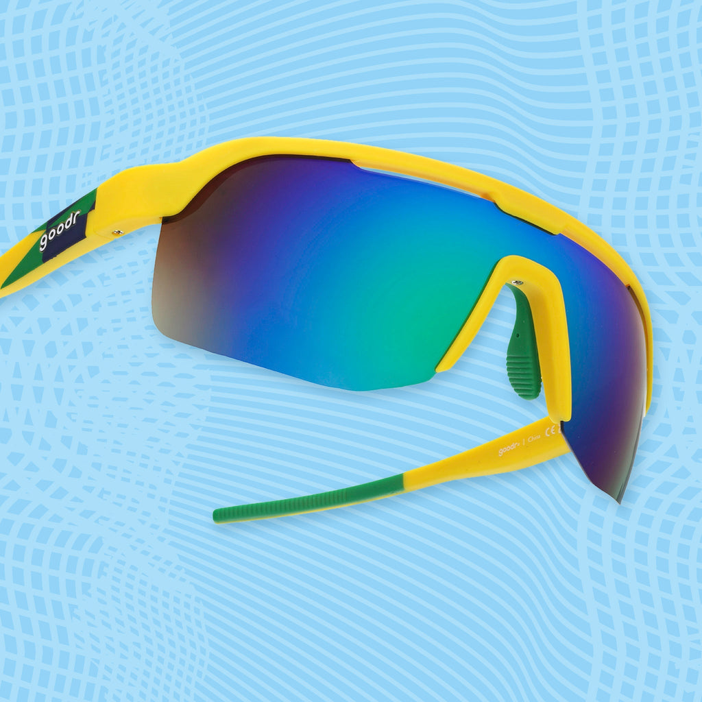 Yellow shield sunglasses with light green mirrored lenses on a blue patterned background.