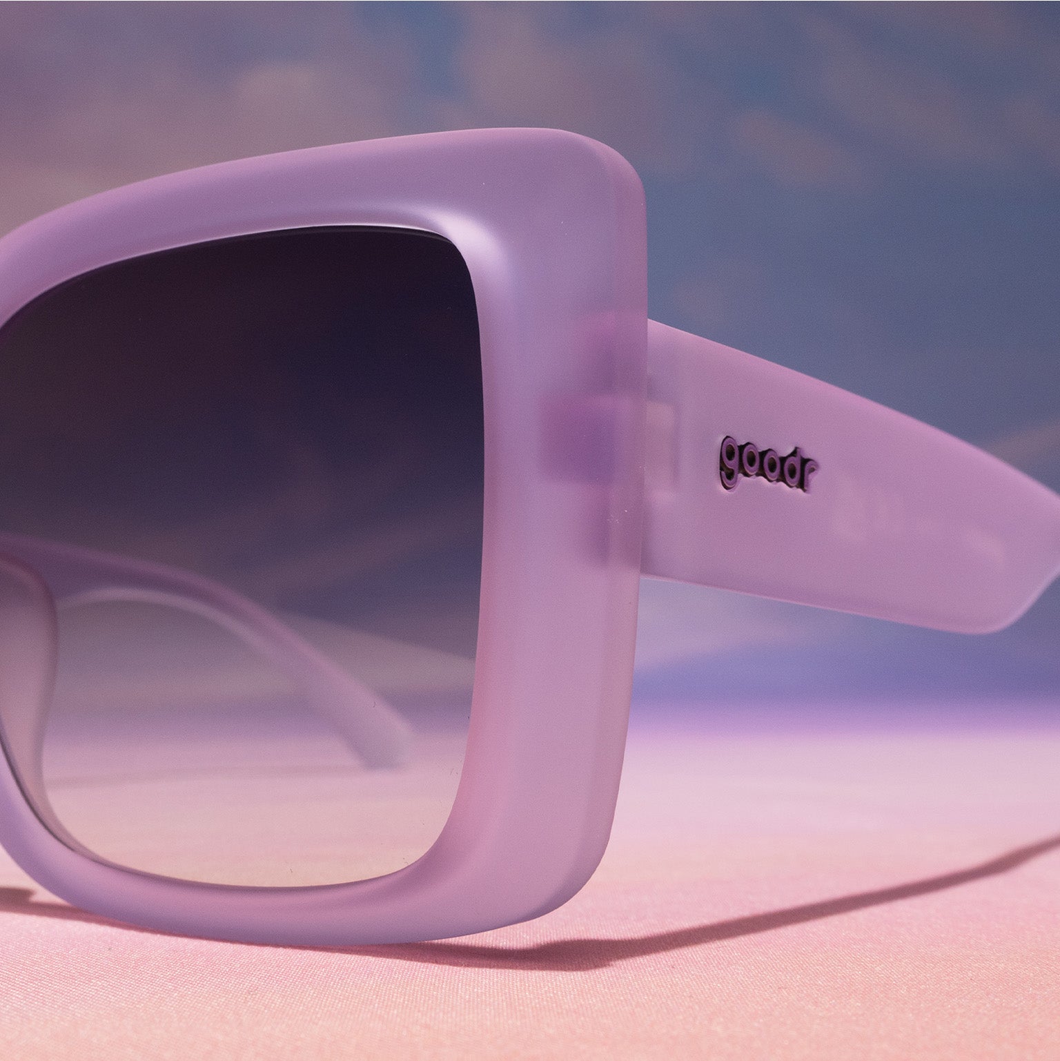 Close-up view of the corner temple of a pair of translucent, pale purple, oversized square Amp G sunnies.