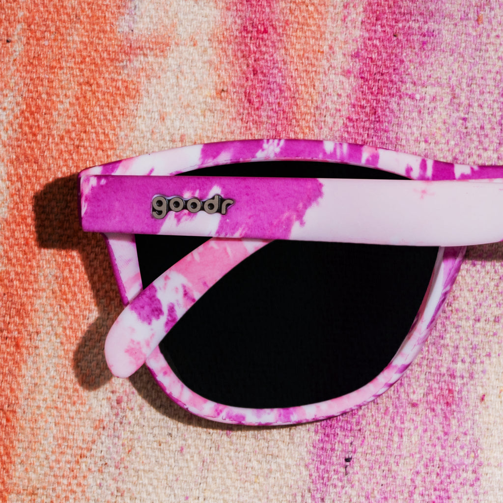 Close-up shot of purple tie-dye sunglasses photographed from behind, sitting on a vibrant tie-dye fabric backdrop.