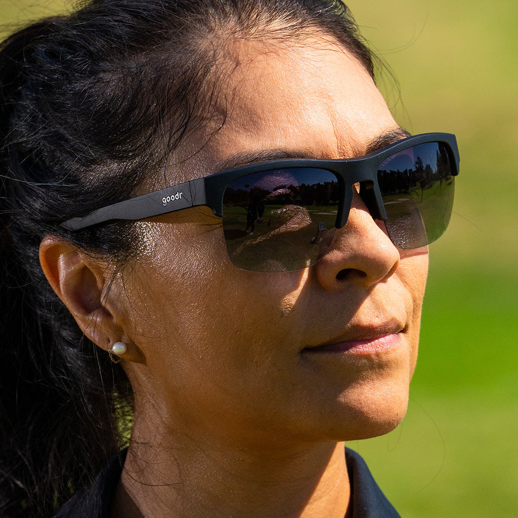 Close-up of a woman outdoors, sweating while wearing black half-rim sunglasses with polarized black gradient lenses.