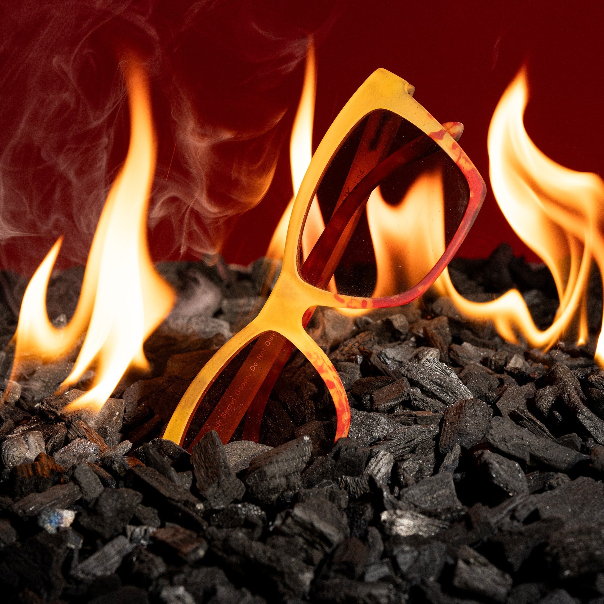 Translucent yellow-orange sunglasses against a backdrop of glowing burning coals.