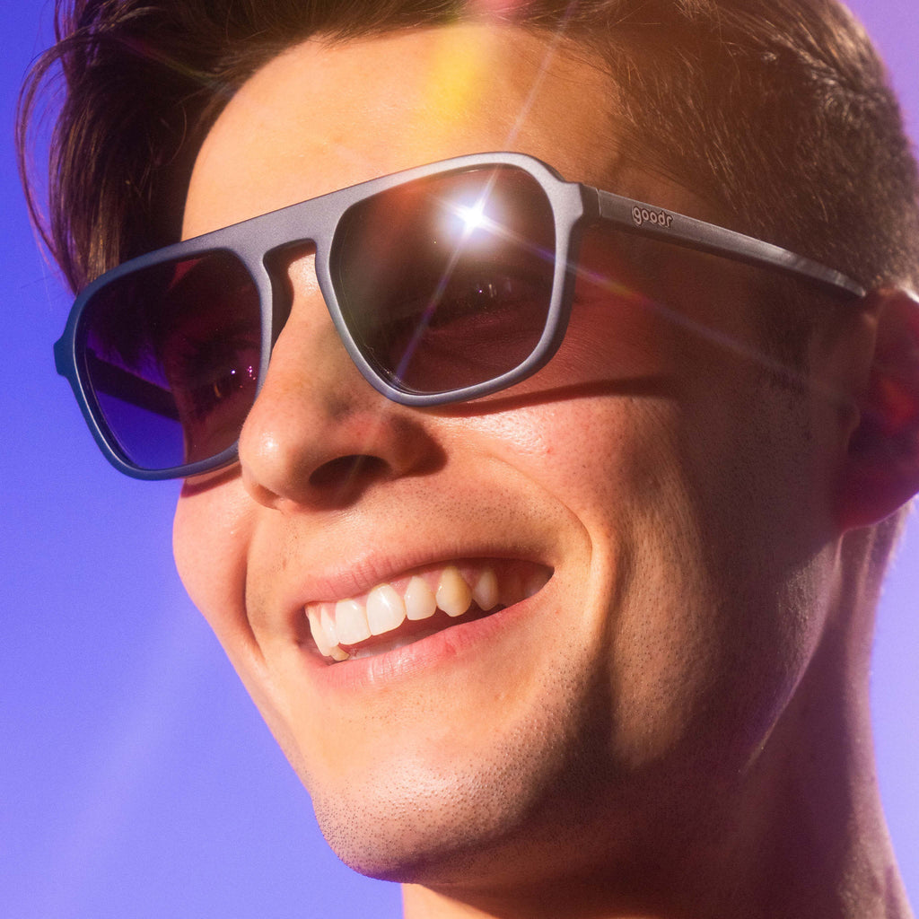 Man wearing black square-shaped goodr sunglasses on a purple background