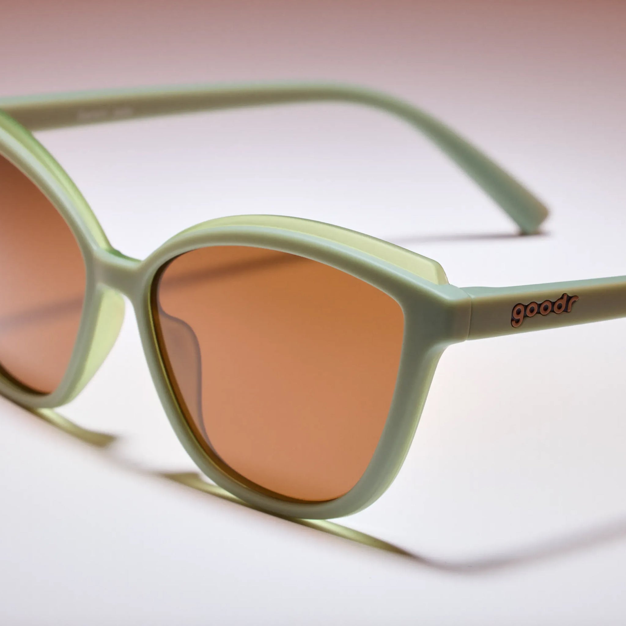 Sunglasses with green frames and brown lenses on a light background