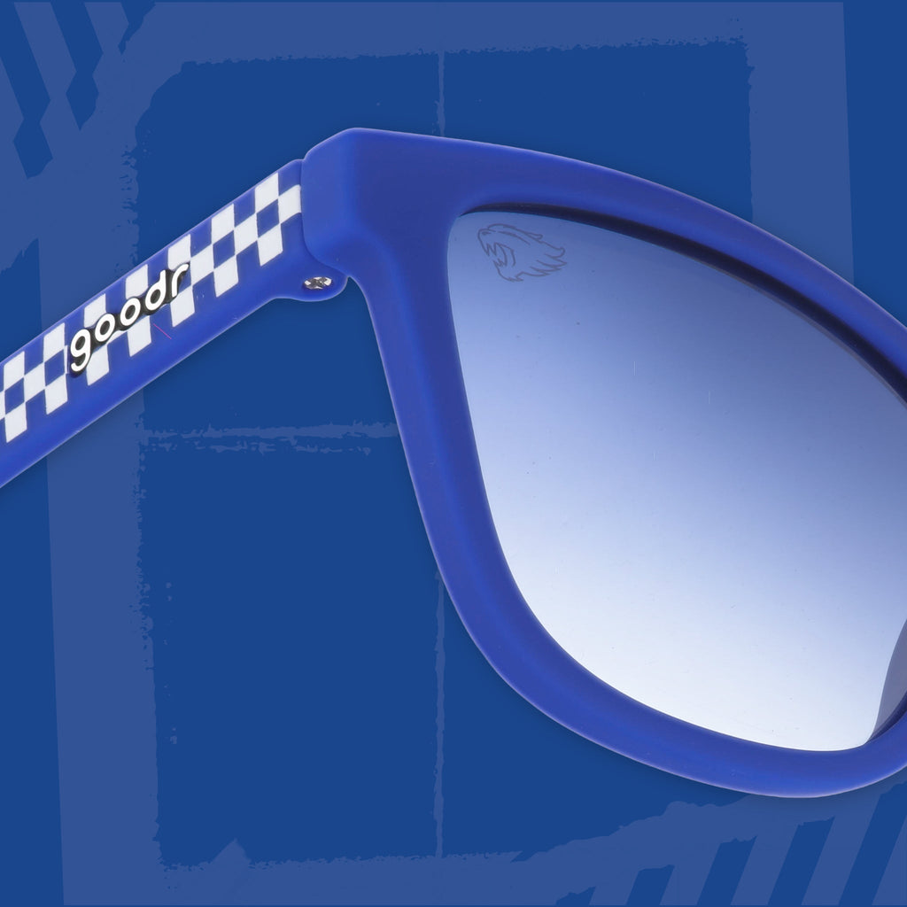 Close-up three-quarter angle view of blue and white checkered sunglasses featuring blue gradient lenses and goodr logo on a blue background.