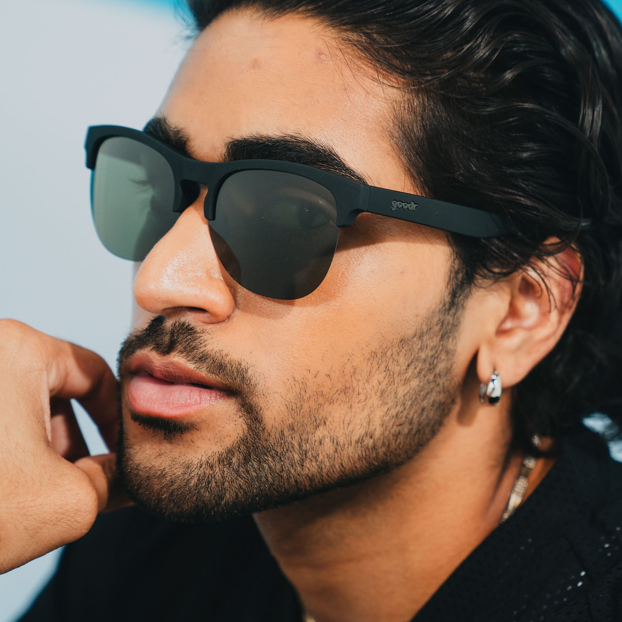 A man wearing matte black half-rim sunglasses with dark green non-reflective lenses poses for the camera.