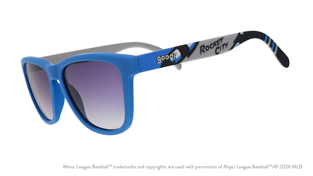 Three-quarter angle view of sunglasses tilted down. Blue frames w/ Rocket City on temples + black gradient lenses.