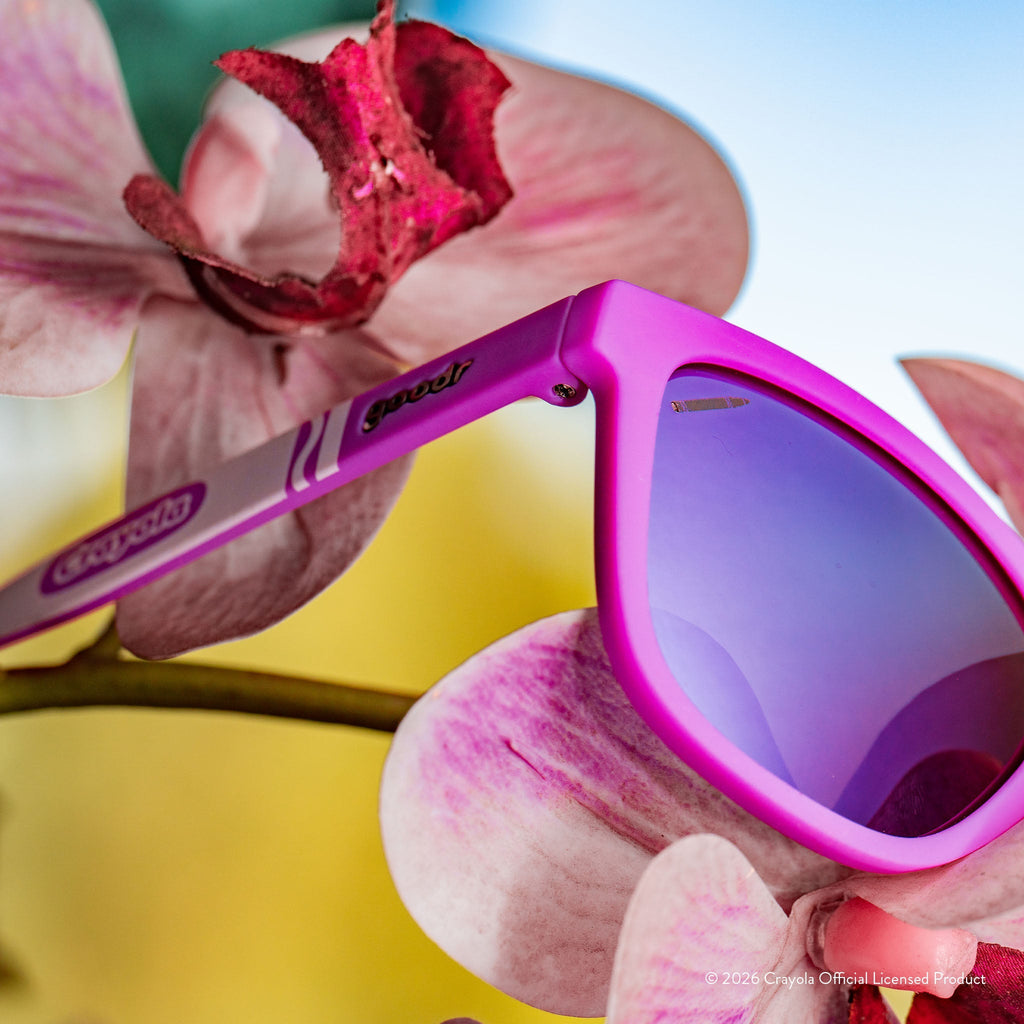 Close-up angled view of magenta sunglasses w/ purple pink reflective lenses+small crayon etching in top corner of lens.