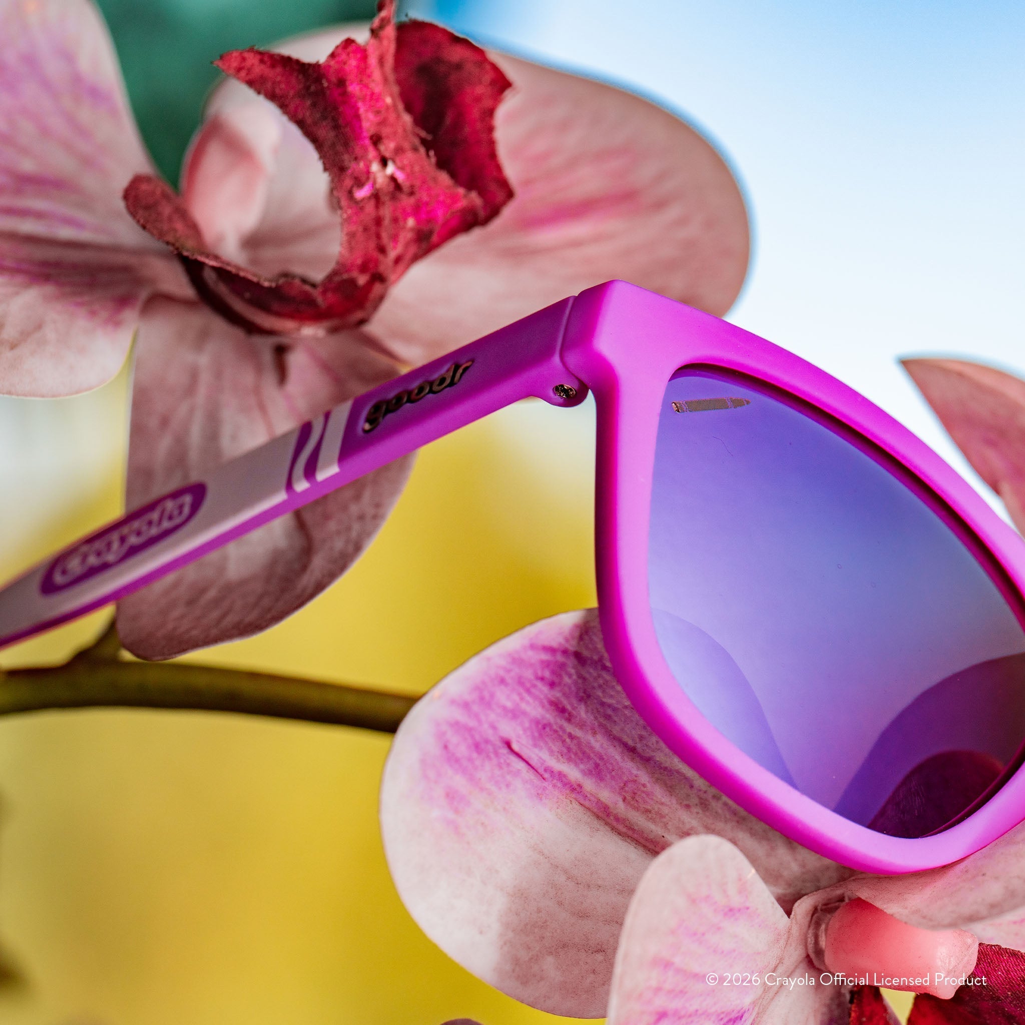 Close-up angled view of magenta sunglasses w/ purple pink reflective lenses+small crayon etching in top corner of lens.