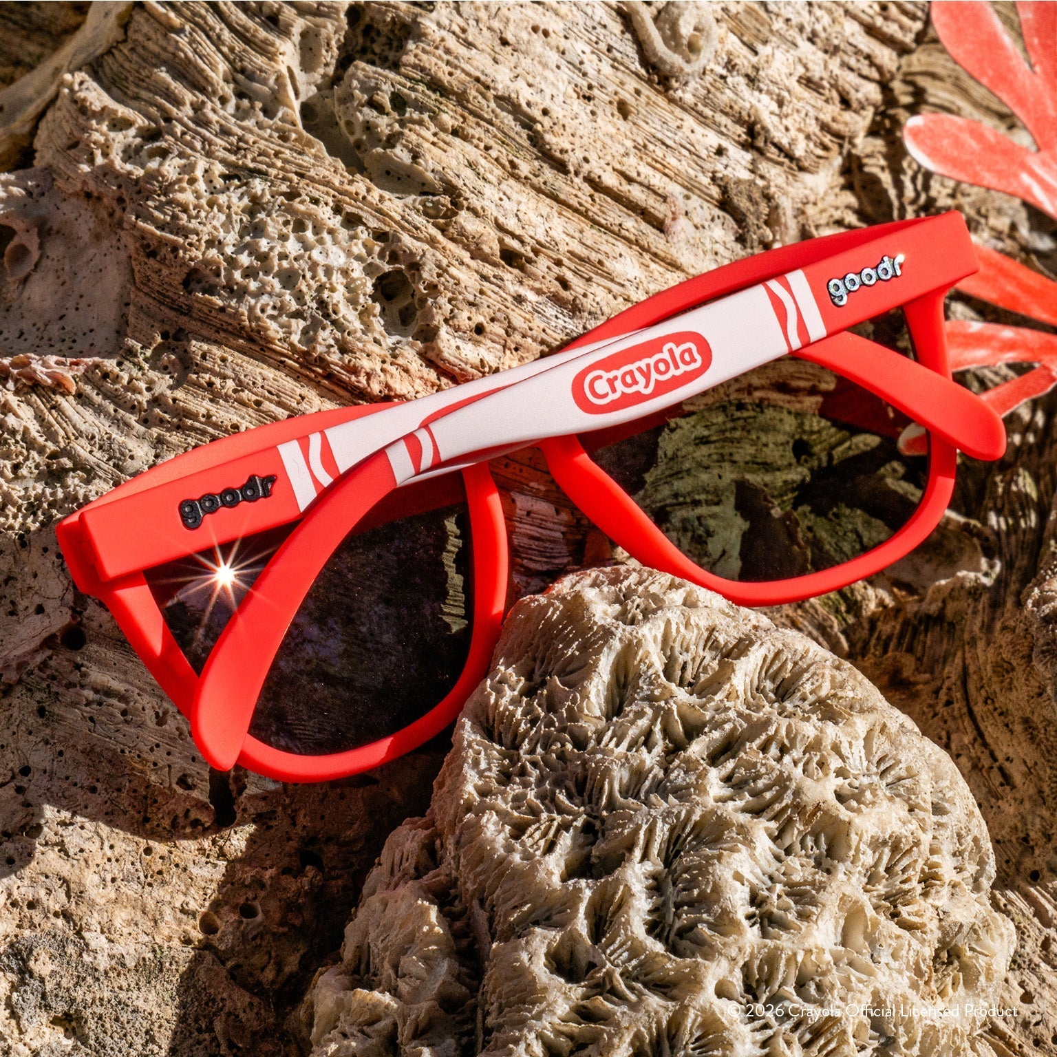Back view of folded coral sunglasses w/ white Crayola marker pattern+burnt orange reflective lenses on a reef.
