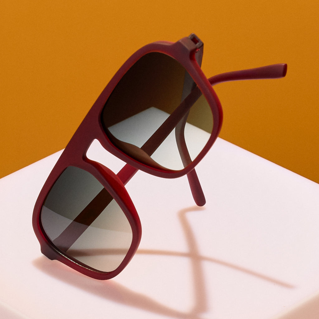 Red sunglasses with dark lenses on a white surface against an orange background