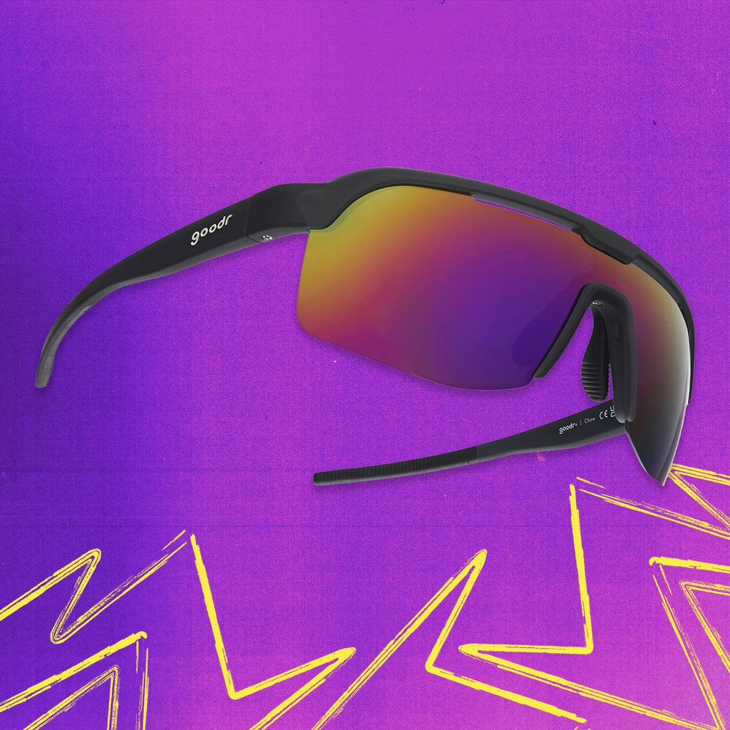 Three-quarter angle view of black shield sunglasses with purple reflective wrap lenses tilted up on a purple background.