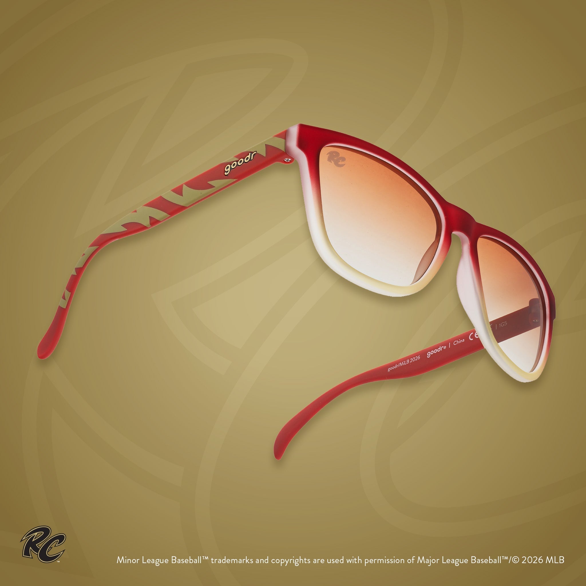 Three-quarter angle view of sunglasses. Brown + red frames w/ amber gradient lenses. RC etching on top of lens.