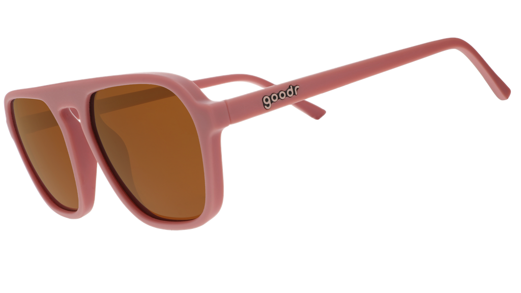 A pair of dusty rose pink goodr sunglasses with muted orange lenses on a white background.