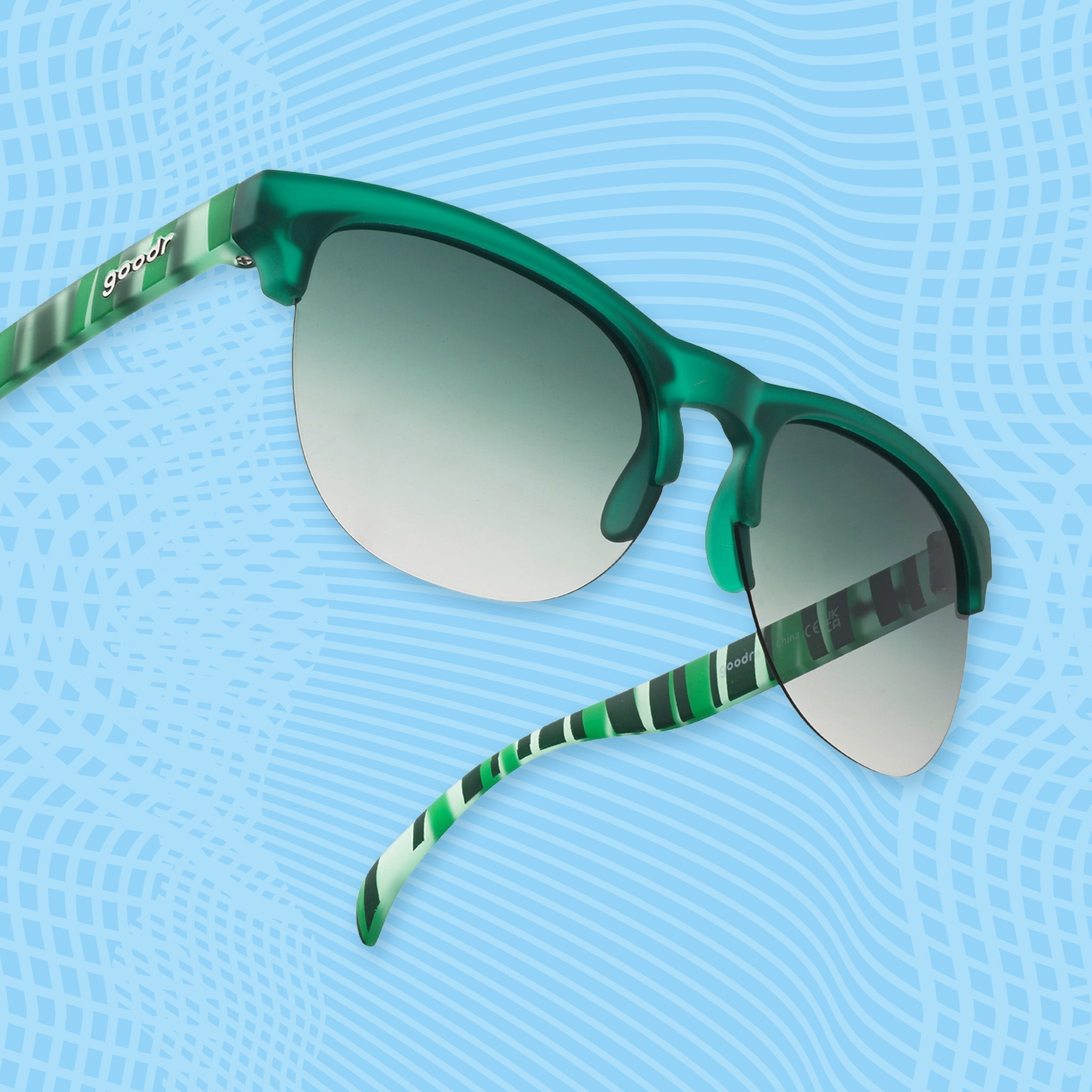 Green translucent sunglasses with mirrored lenses and striped temple arms on a blue patterned background.