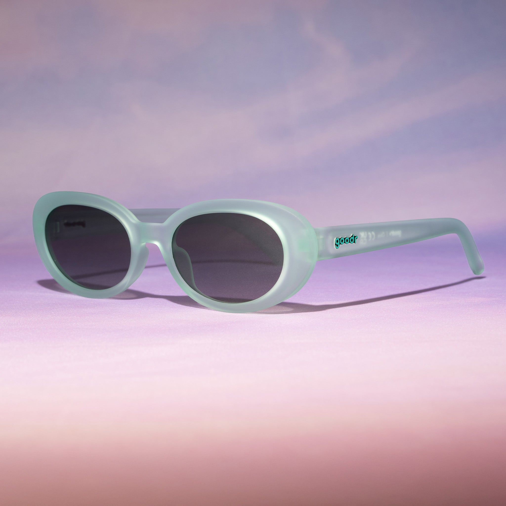 Three-quarter angle view of translucent pale green oval Beat G shades sitting on a peachy backdrop reminiscent of a sunset.