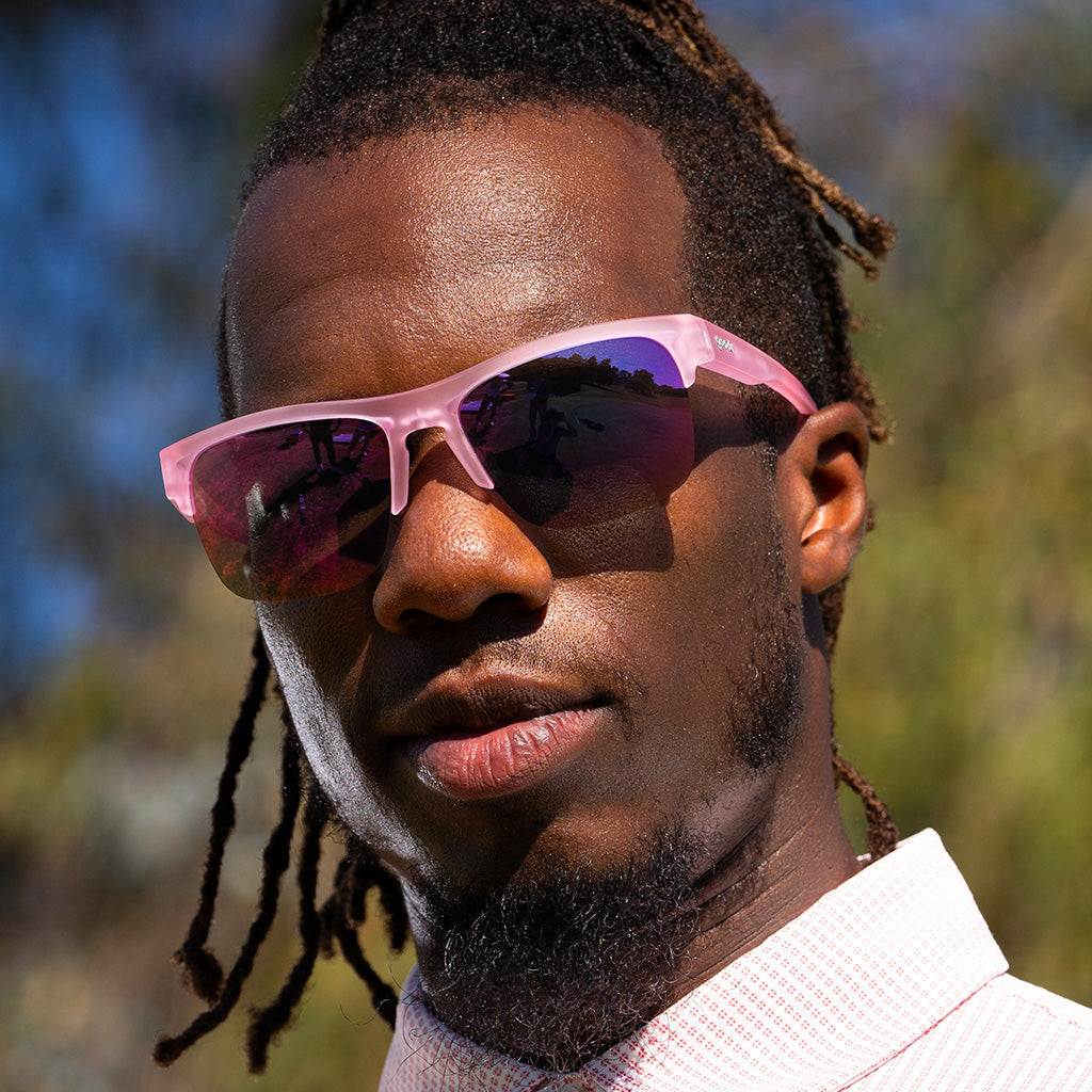 Close-up of a man outdoors wearing half-rim translucent pink sunglasses with pink reflective polarized lenses.