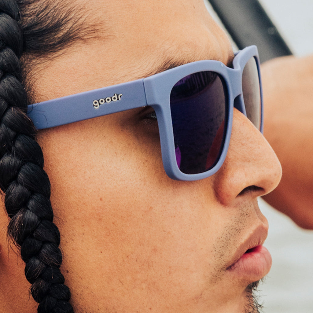 Side view of a young man with braids wearing dark blue sunglasses with dark blue lenses designed to float in water.