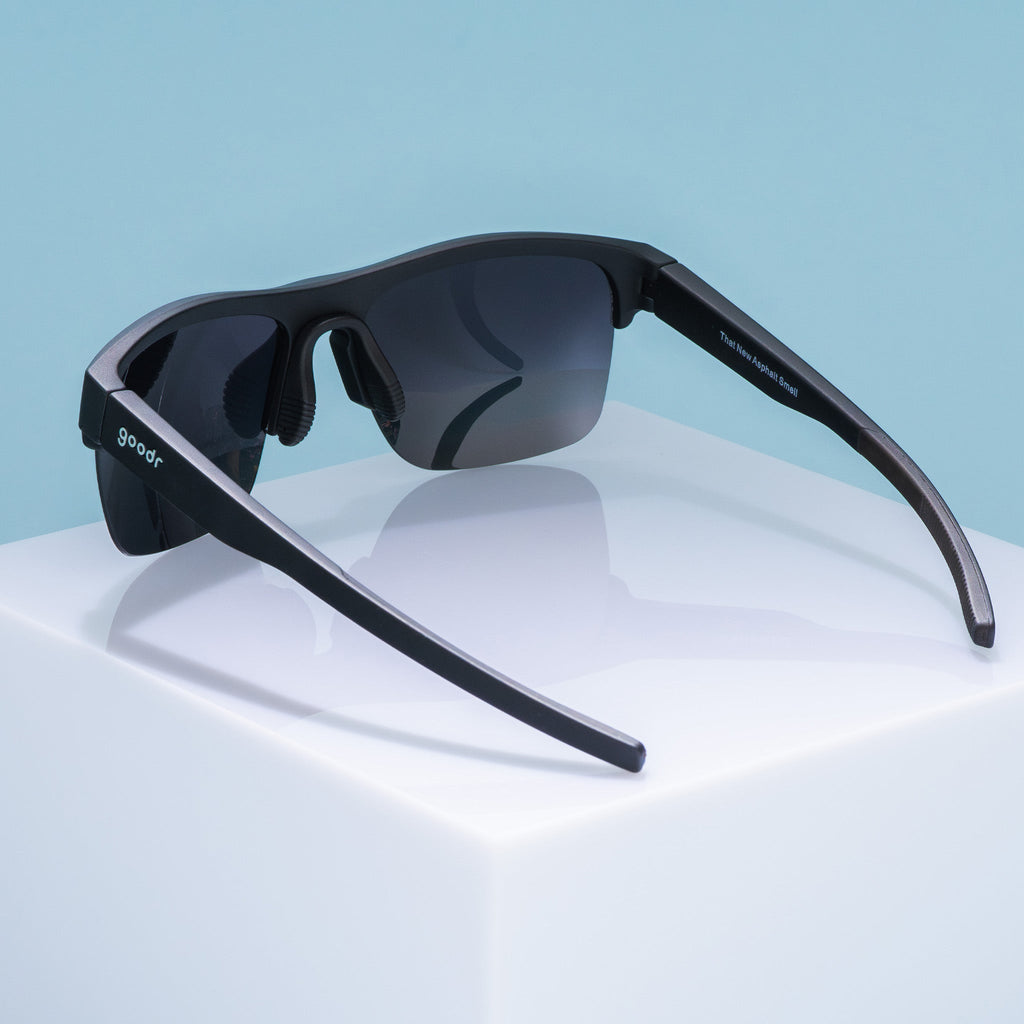 Three-quarter back angle view of black half-rim sunglasses featuring polarized black gradient lenses. The arms of the sunglasses are fully extended, showcasing an adjustable nose piece and the goodr logo on the outer left arm.