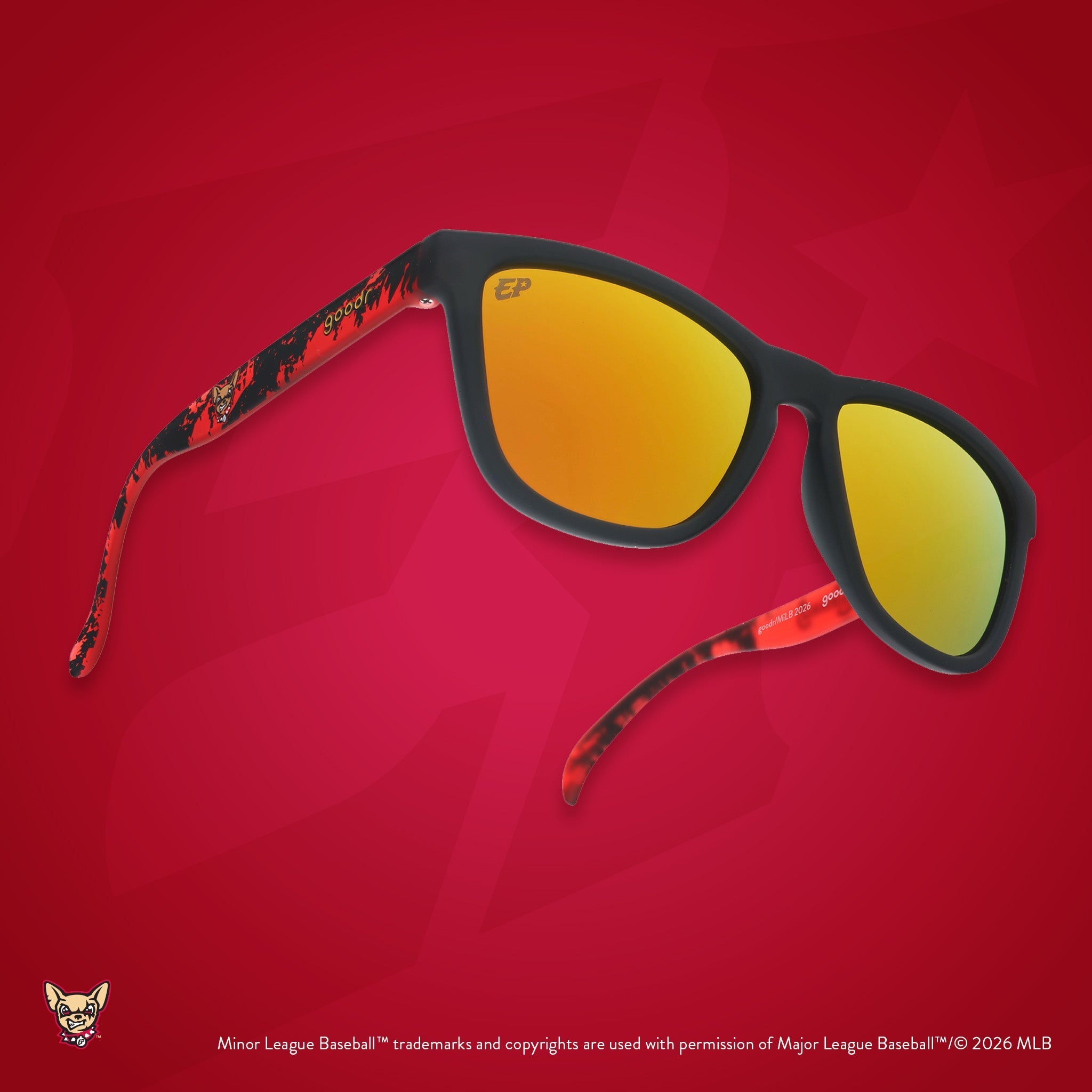 Three-quarter angle view of tilted shades. Dark gray+red frames w/ Chihuahuas logo on temples. Amber reflective lenses.