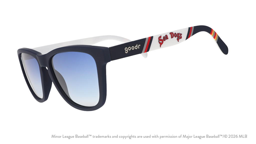 Three-quarter angle view of sunglasses. Dark blue frames w/ Sea Dogs on temples + blue gradient lenses.