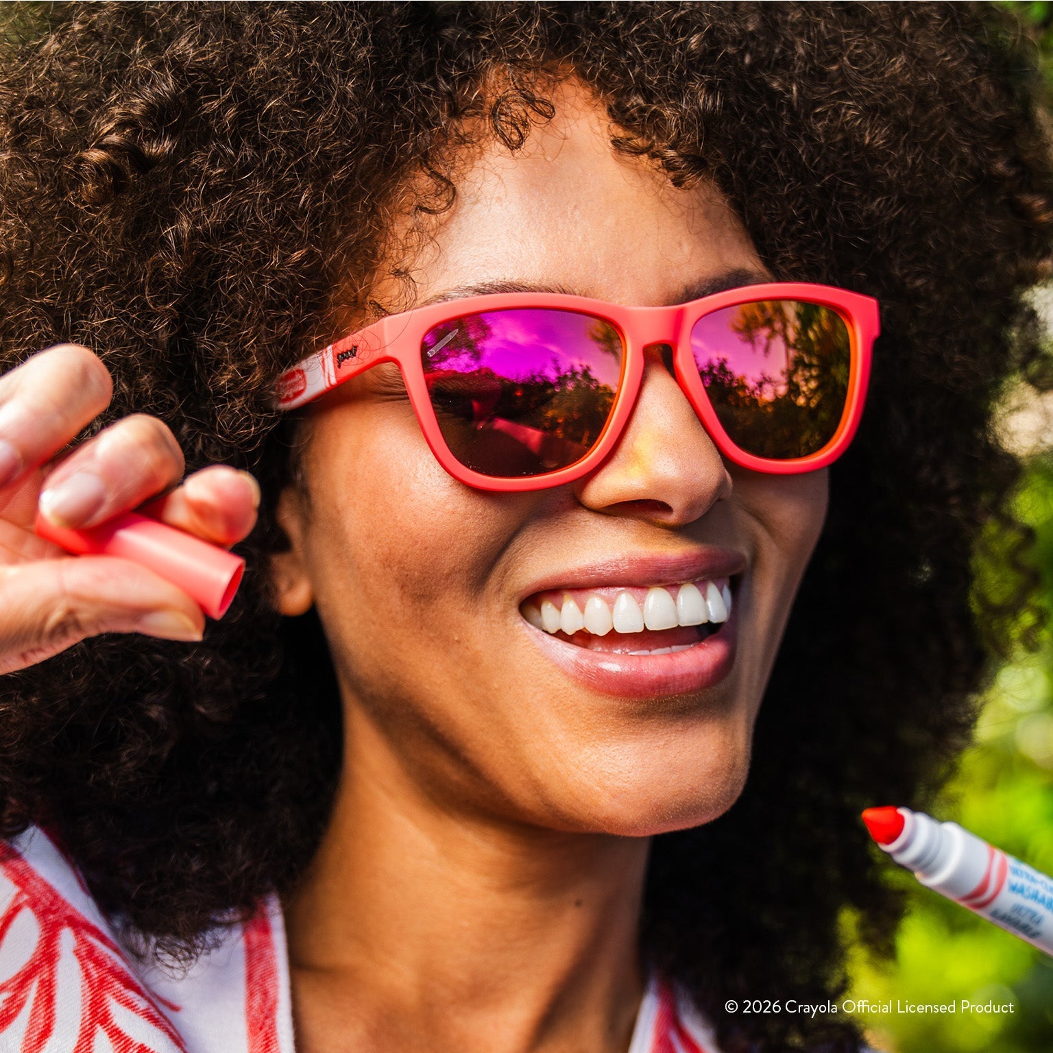 Woman smiling while wearing coral sunglasses w/ white Crayola marker pattern+ burnt orange reflective lenses.