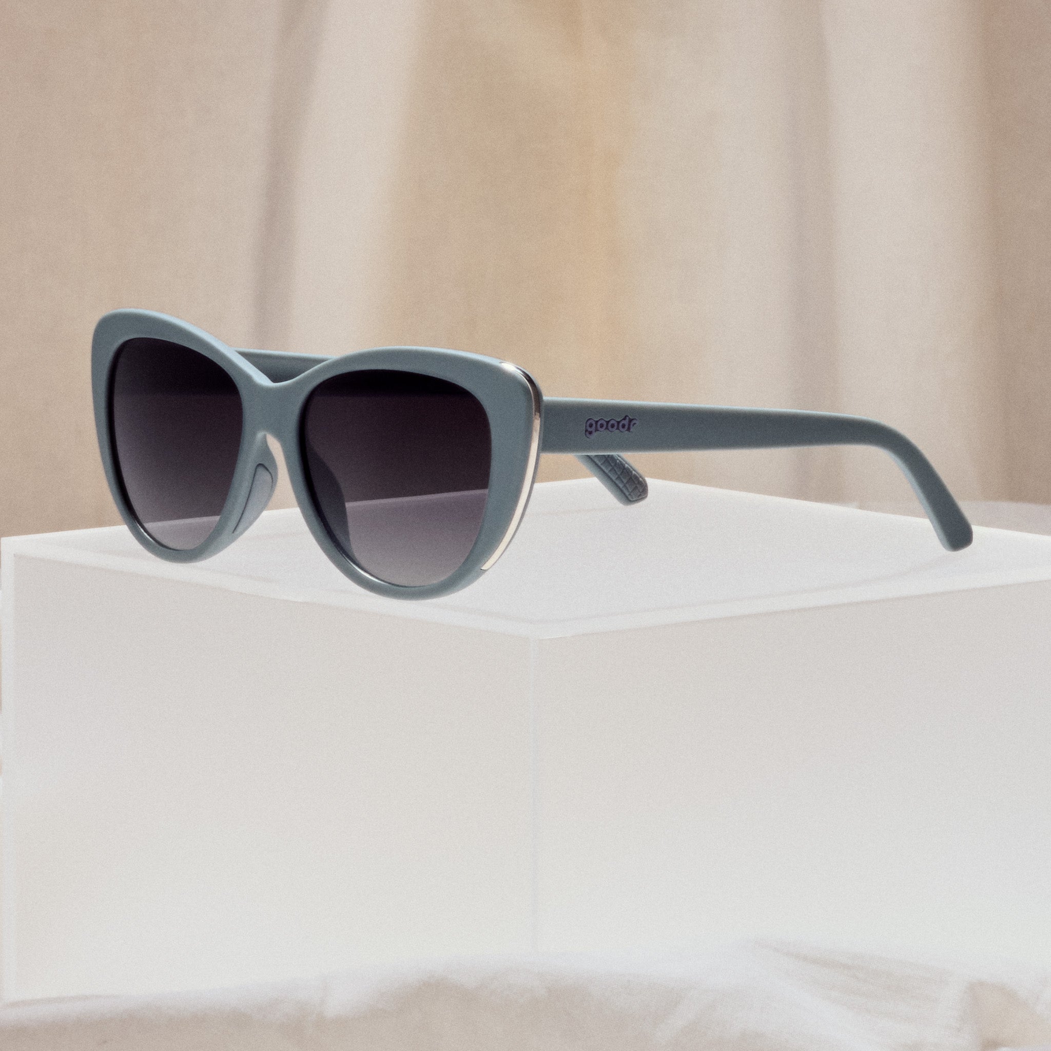 A pair of grey cat eye sunglasses with dark lenses and gold accents on the sides of each frame.