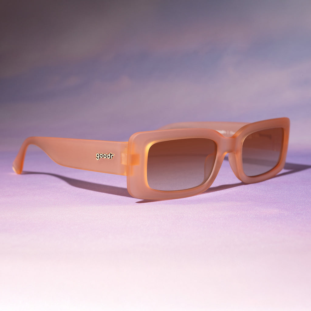 Three-quarter view of translucent peach rectangular Luxe Gs sitting on a purplish-pink backdrop reminiscent of a sunset.