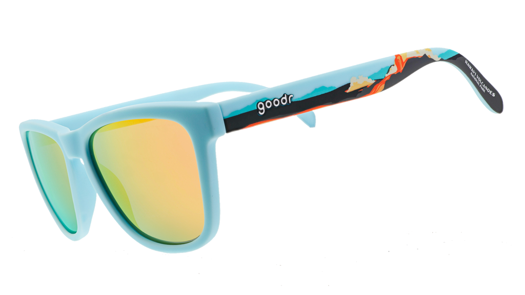 Pair of sunglasses with light blue frames and reflective yellow-orange lenses. The arms feature a vibrant tropical design with illustrations of waves and a sunset gradient.