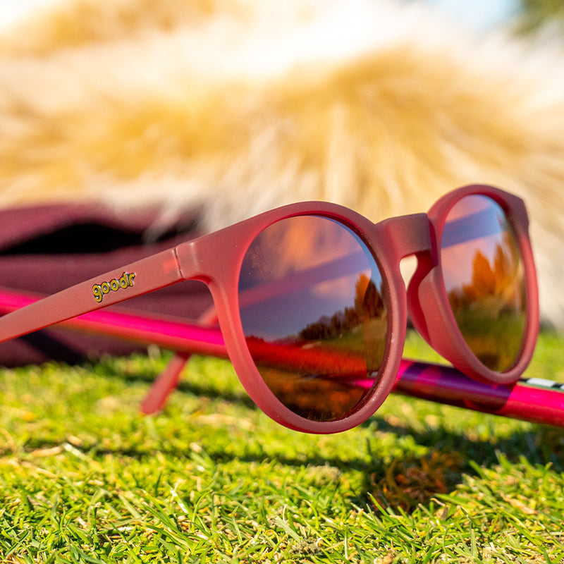 Three-quarter angle view of round burgundy sunglasses with brown lenses sitting on course, a furry collar behind it.