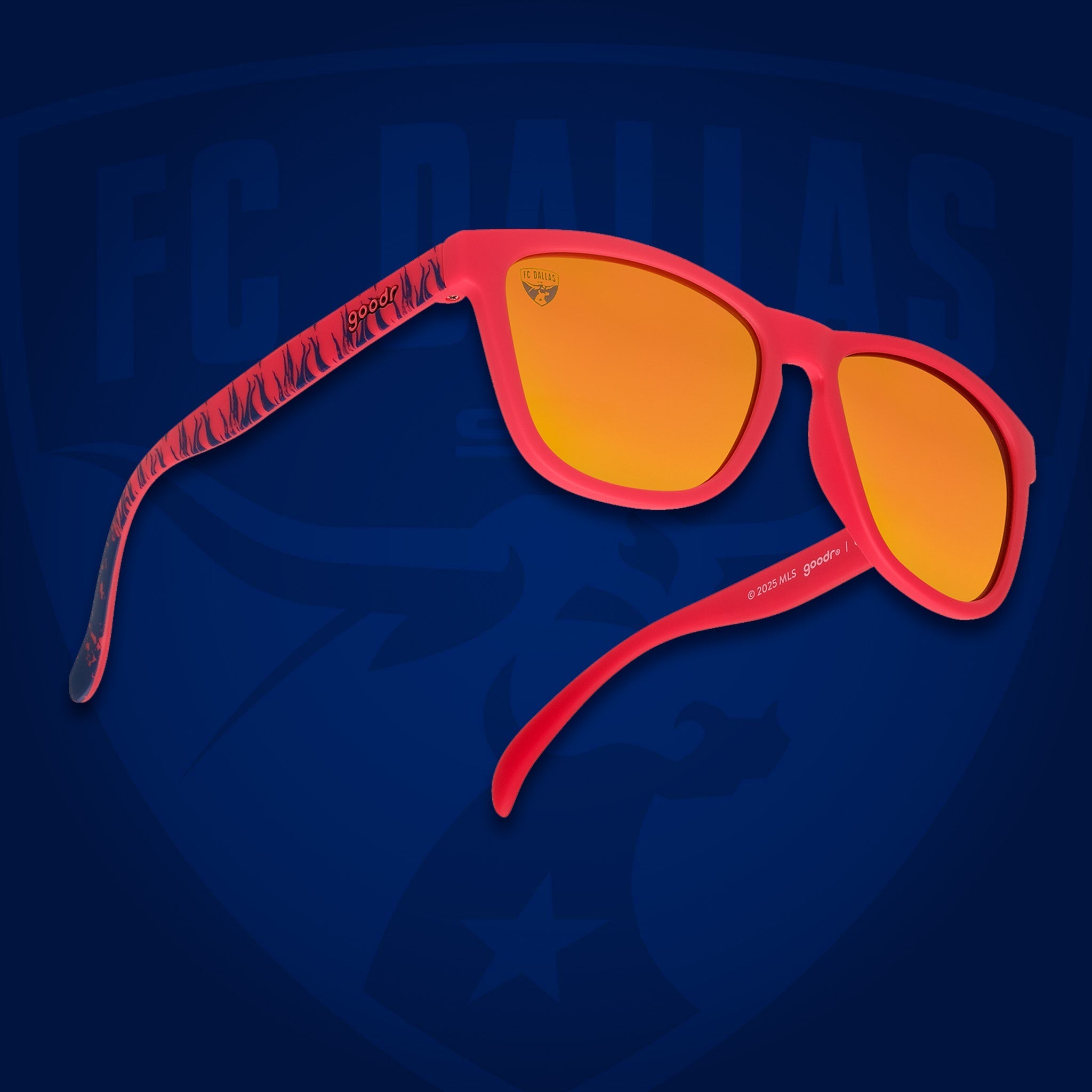Three-quarter angle view of shades tilted up. Red frames w/blue flames+FC Dallas on temples. Amber reflective lenses.