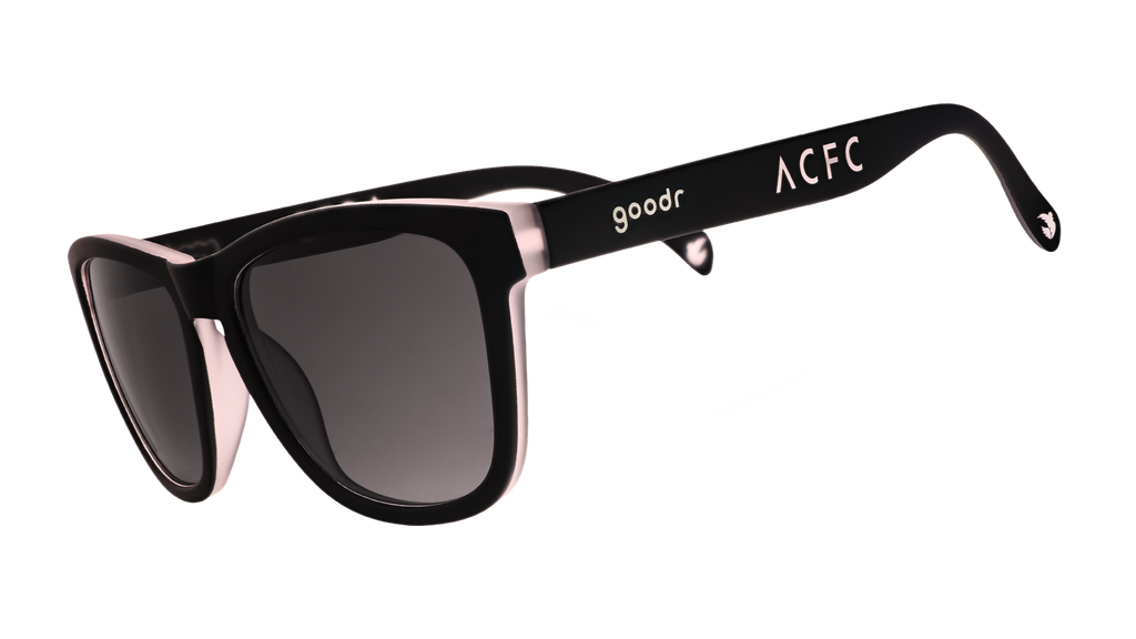Three-quarter angle view of black and pink sunglasses with black gradient lenses and ACFC logo.