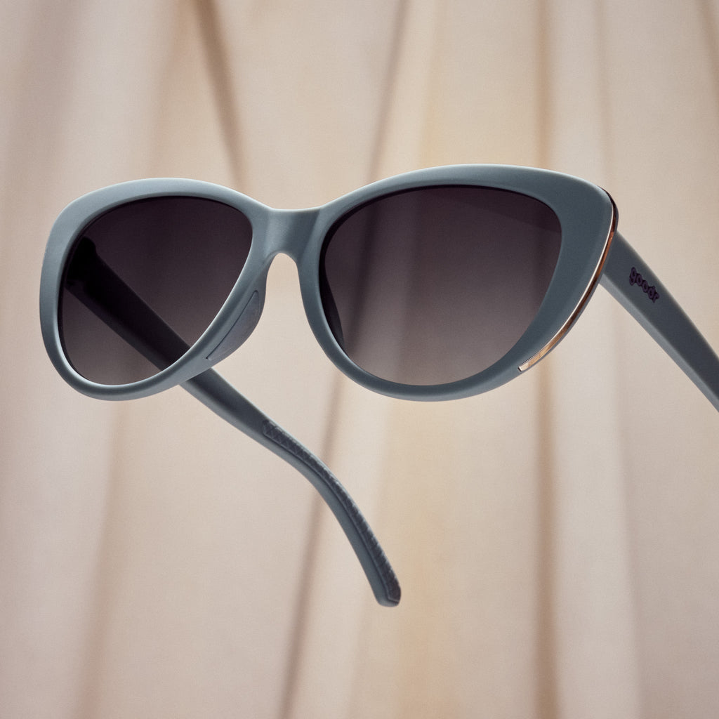 A pair of black cat eye sunglasses with dark lenses and gold accents on the sides of each frame.
