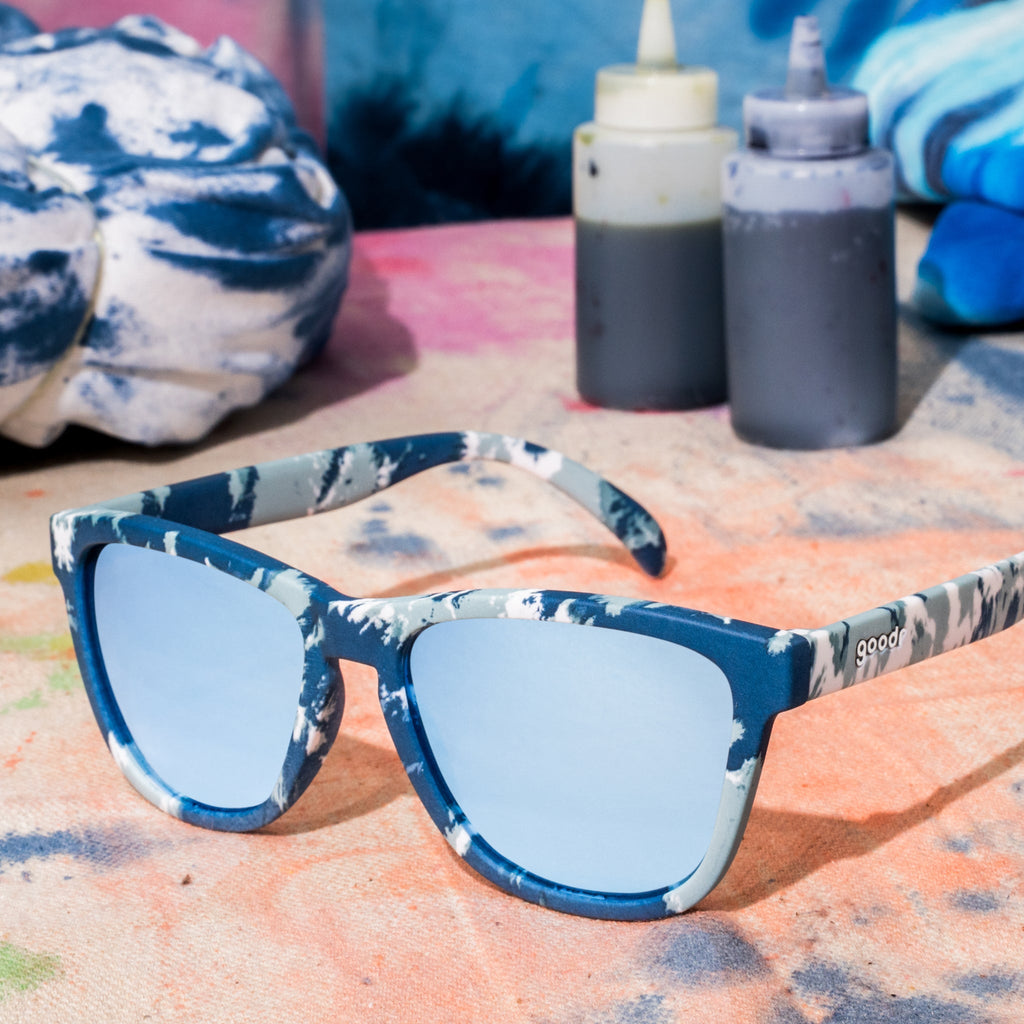 Blue tie-dye sunglasses sitting on a ball of white fabric tied with rubber bands, in the process of being tie-dyed blue.