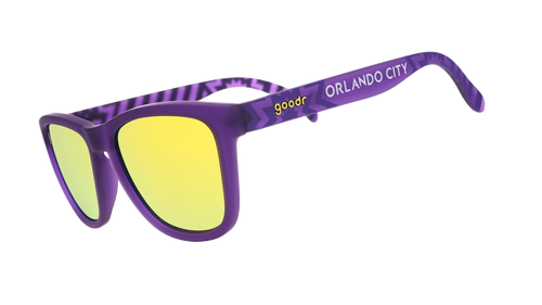 Angled view of shades tilted down. Purple frames w/ stripes + Orlando City on temples. Violet reflective lenses.