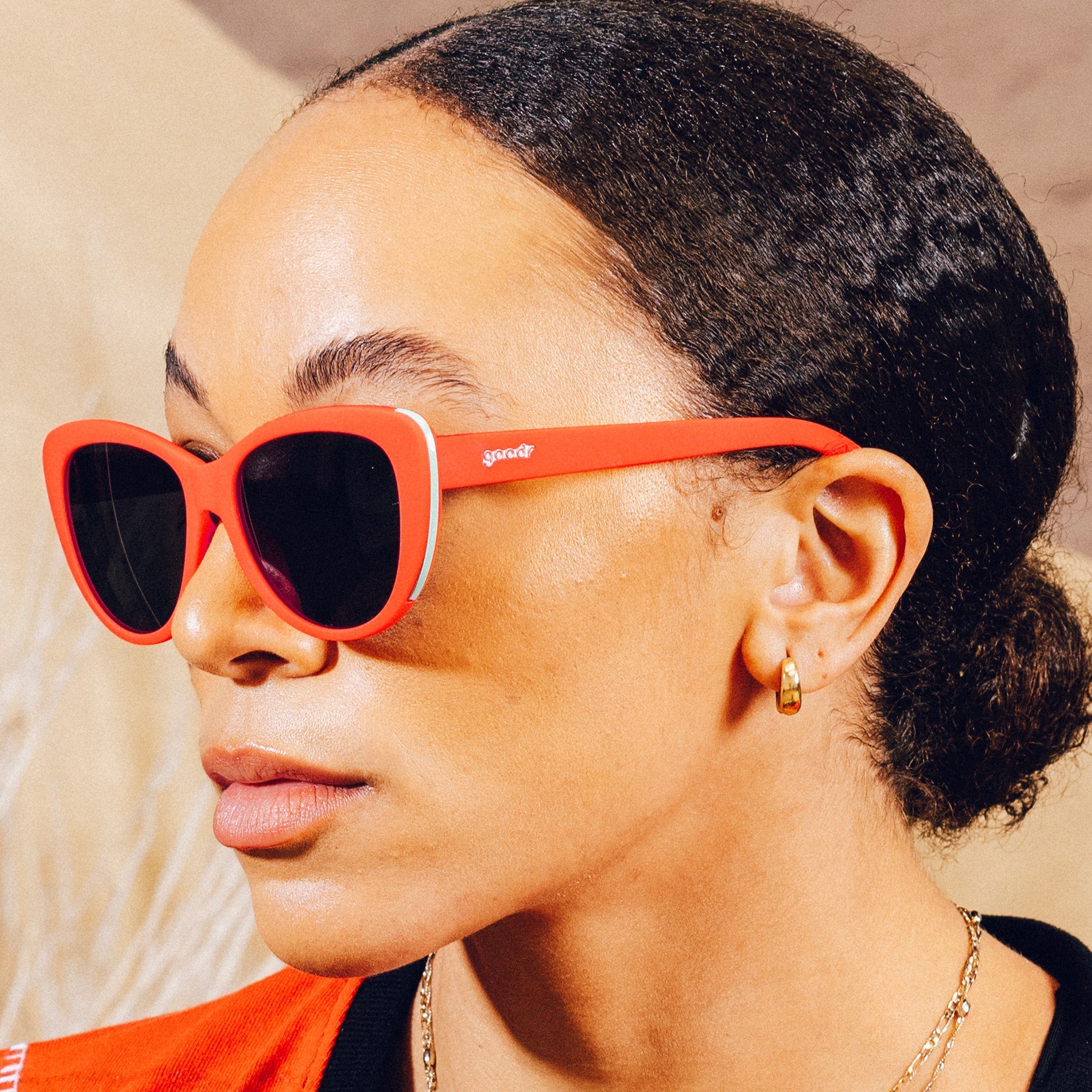 Side profile of a woman wearing red cat-eye sunglasses with black non-reflective lenses in front of a desert backdrop.