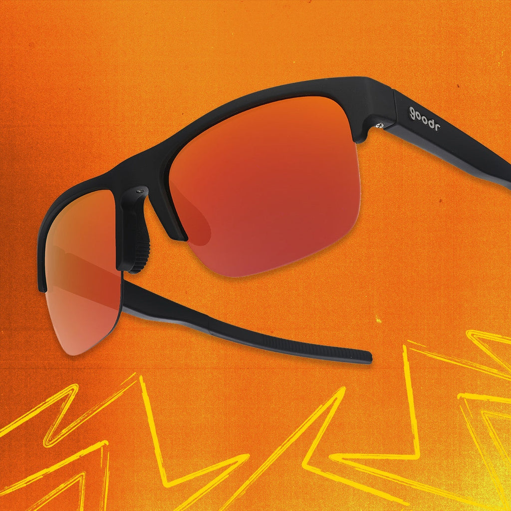Three-quarter angle view of black shades w/ half-rim frames+orange reflective lenses tilted up on an orange background.