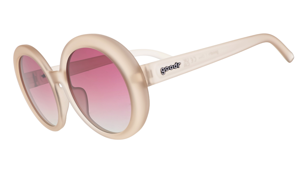 Three-quarter angle view of oversized round beige sunglasses with purple gradient lenses against a white background.