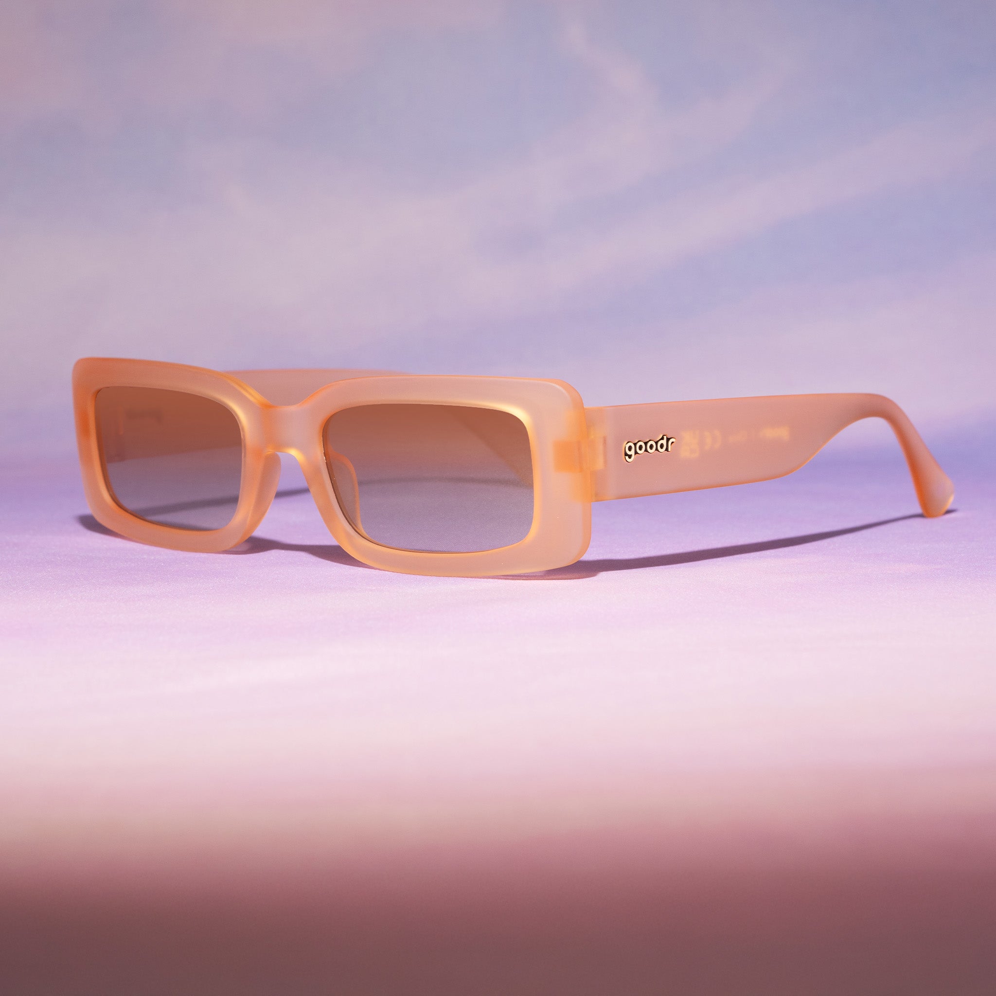 Three-quarter view of translucent peach rectangular Luxe Gs sitting on a purplish-pink backdrop reminiscent of a sunset.