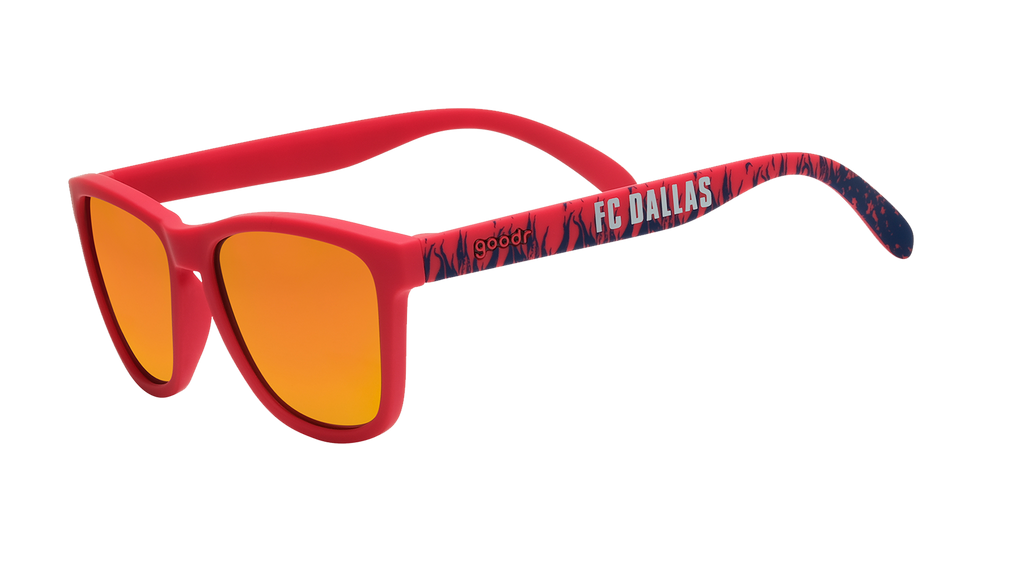 Three-quarter angle view of shades tilted down. Red frames w/blue flames+FC Dallas on temples. Amber reflective lenses.