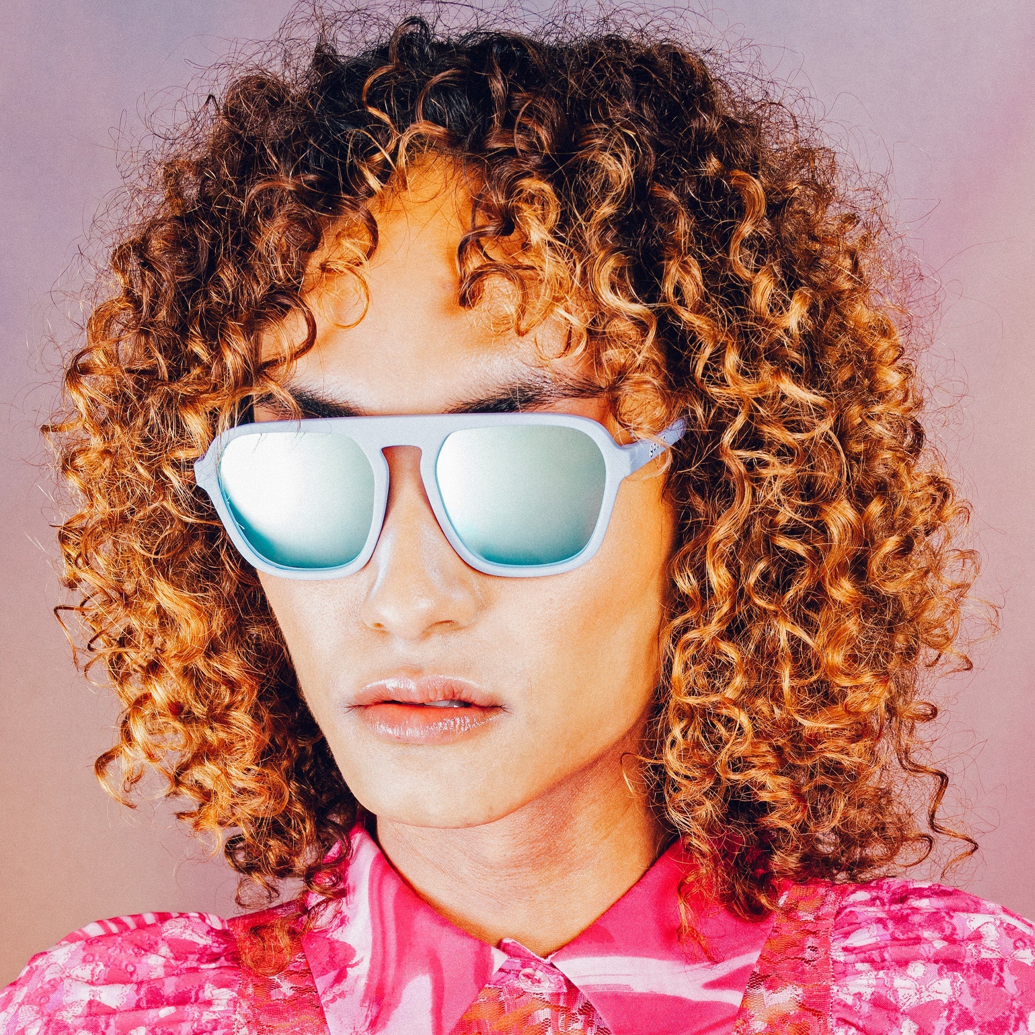 Woman poses while wearing light blue retro-inspired aviator sunglasses with blue reflective lenses.
