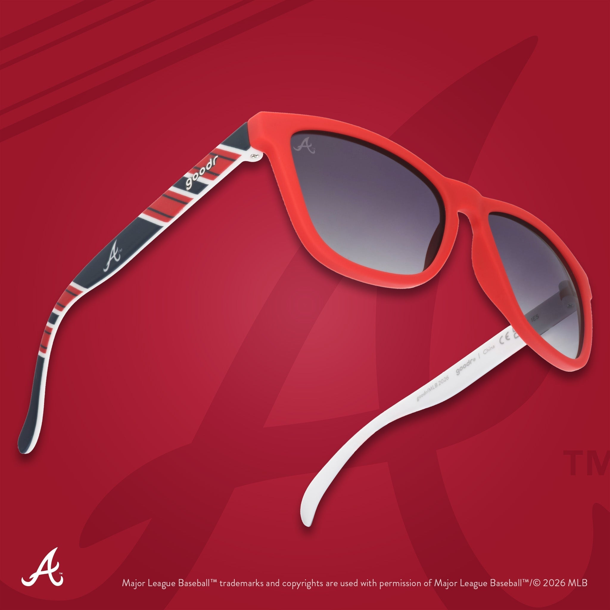 Three-quarter angle view of a pair of red, white, and navy Braves sunnies floating against a red background featuring the A.
