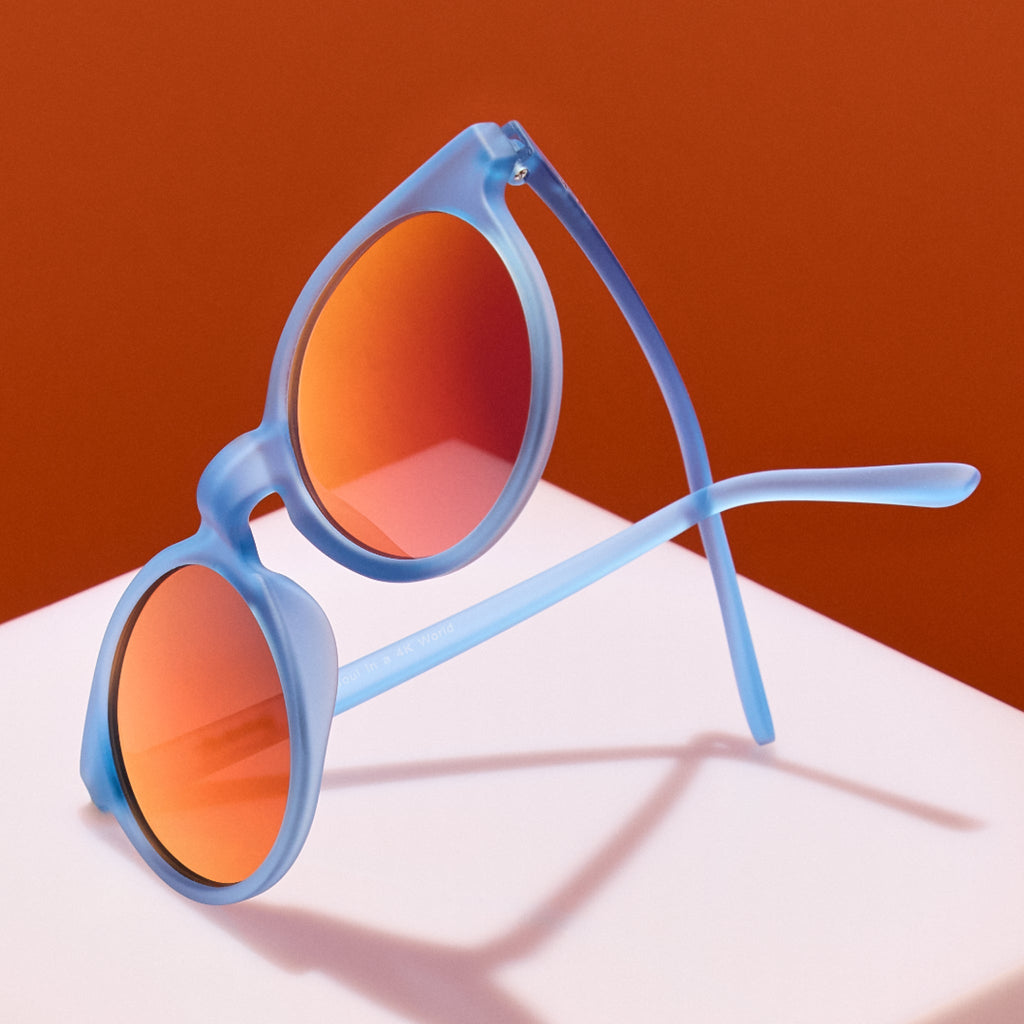 Blue sunglasses with orange lenses on a white surface against an orange background